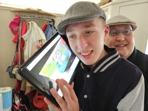 Twee mannen, één met een tablet, glimlachen in een kleurrijke kamer.